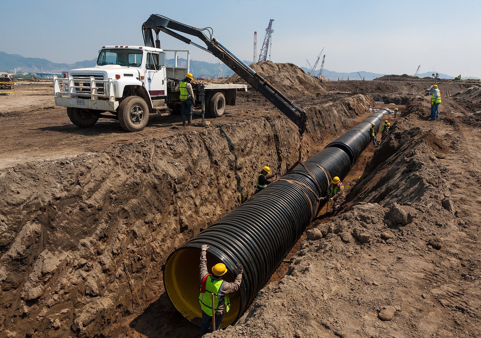 Excavator and crew laying pipe in a long open trench