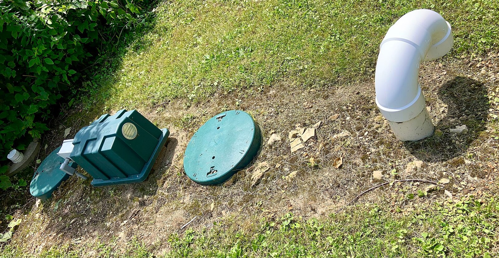 Green septic tank access lids and a white vent pipe in a lawn